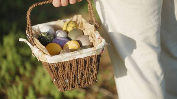 istock A young woman holds a woven basket with decorated Easter eggs in her hands, in a forest against the backdrop of green grass. 1871777918