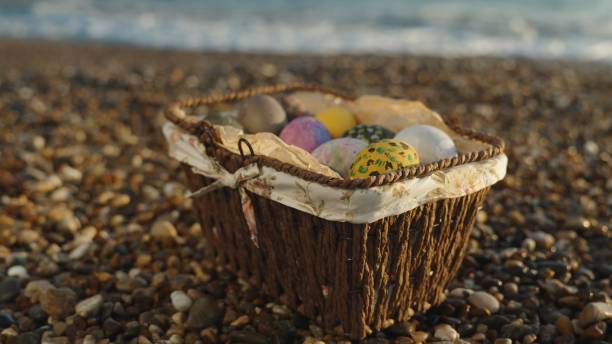 una cesta de mimbre con huevos de pascua en las rocas junto al mar. puesta del sol - easter holiday feast day yellow fotografías e imágenes de stock