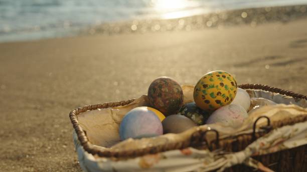 istock Wicker basket with Easter eggs on the beach by the sea. Close-up, sun rays and waves. 1871778445