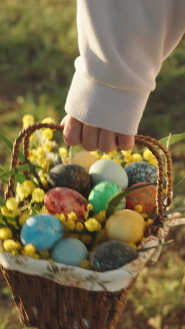 Vertical video. A walk behind a woman in white carrying a basket of painted Easter eggs. Sunny forest at dawn.