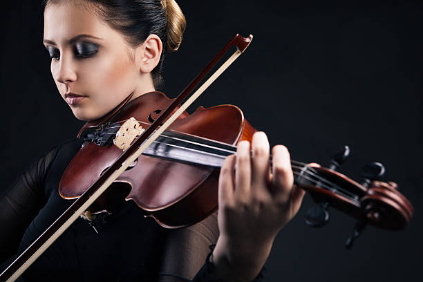 istock Beautiful young woman playing violin over black 187181994