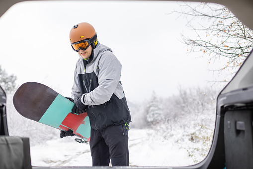 Man taking snowboard out of car trunk on snowy mountain