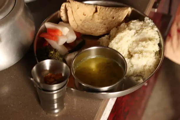 Photo of A steel plate thali with Normal Indian Staple food including radish, carrot, rice, chapati, daal, gajak, steel glass