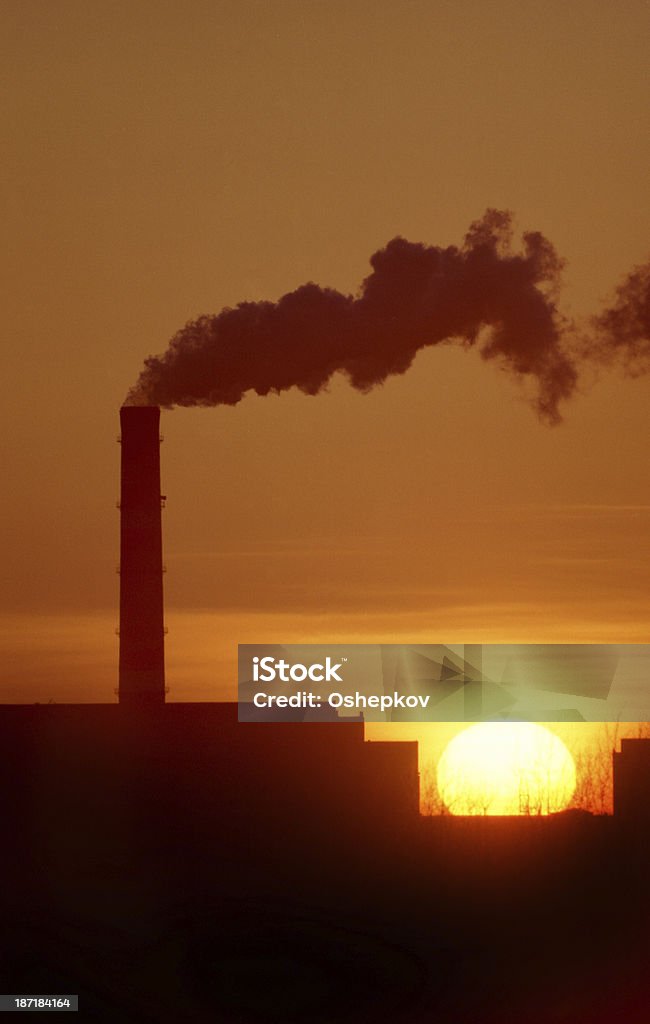 Chimneys and smoke against the setting sun. Chimneys and smoke against the setting sun. The smoke from the plant. Back Lit Stock Photo