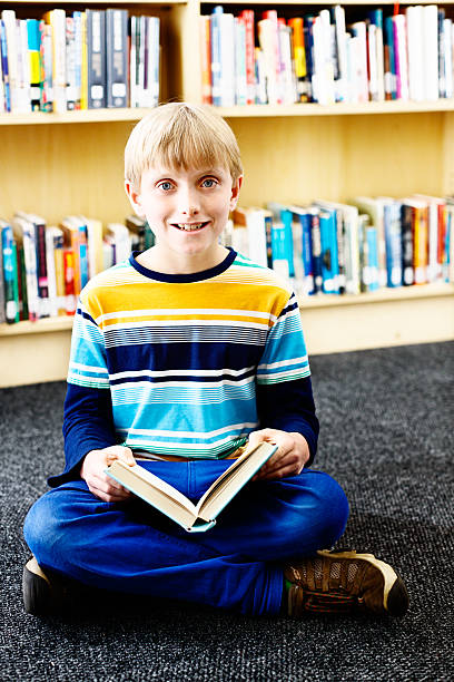 istock Let me read you a story! Smiling schoolboy in library 187184189