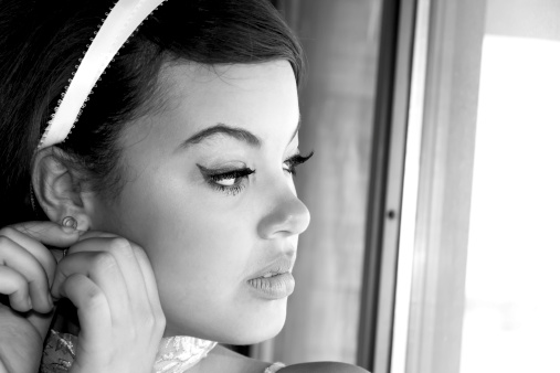 B&W horizontal studio shot on mixed race teen looking out window while adjusting near earring.