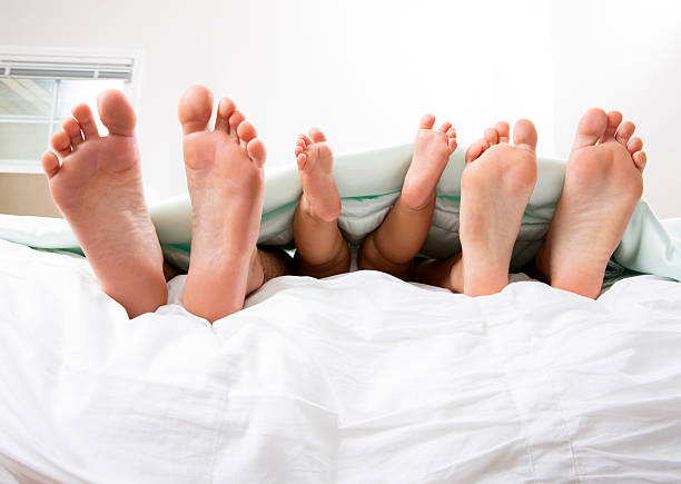 Closeup of family feet in bed This is a photo of a babies feet between her mom and dad on a bed. bed human foot couple two parent family stock pictures, royalty-free photos & images