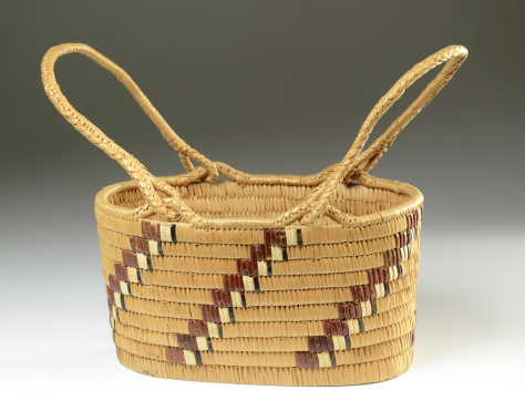 Antique Native American woven basket with handles on a gradient background.