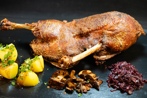 Roast duck leg with mashed green vegetables, beetroot, and pumpkin seeds on light gray background