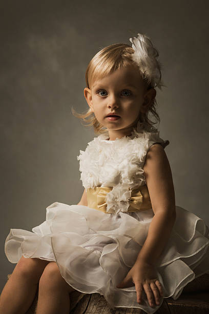 Cute adorable baby girllying alone dressed on a white bed.Little child looking at the camera .Baby learning grab on white background.Portrait of happy daughter. Baby fashion clothes.A child of 5 months is having fun alone,lying on a snow-white bed.