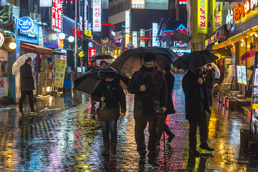 People shopping carrying umbrellas on a rainy evening beneath the neon lit streets of the Myeong-dong shopping district in central Seoul, South Korea.