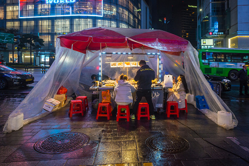 Diners eating at a popular street food stall protected from the rain illuminated at night in the Myeong-dong shopping district of central Seoul, South Korea’ vibrant capital city.