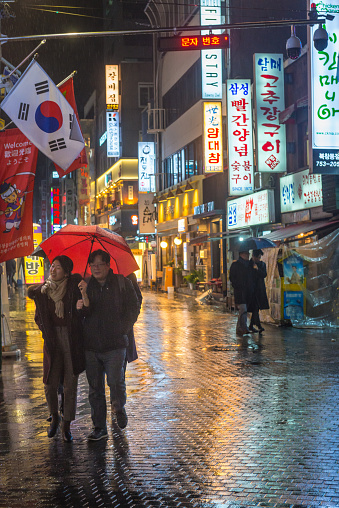 People shopping carrying umbrellas on a rainy evening beneath the neon lit streets of the Myeong-dong shopping district in central Seoul, South Korea.