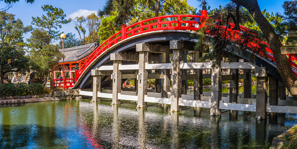 Traditional red wooden arch bridge over tranquil waterway in Sumiyoshi, Osaka, Japan's vibrant second city.