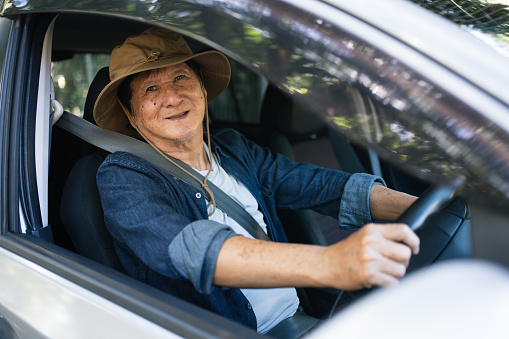 Senior Asian man delights in the joy of driving his car for an adventures experience. Smiling elder Asian man sitting in driver seats and looking at the camera
