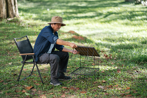 Senior Asian man setting up portable outdoor table in nature