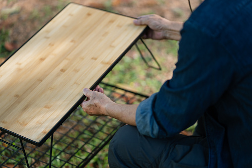 Senior Asian man setting up portable outdoor table in nature