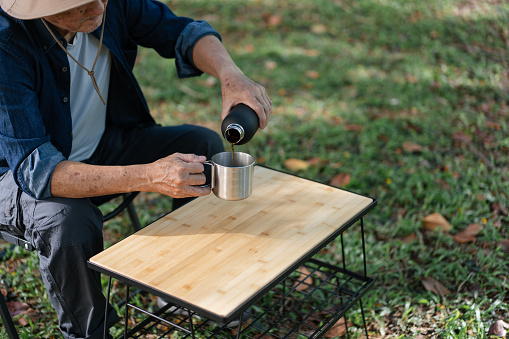 Senior Asian man enjoys coffee preparation on his outdoor table