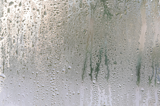 Window glass with steam condensation and drops after or during rain, wet glass as background or texture
