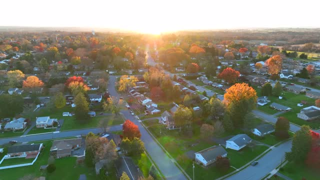 Small town in USA. Colorful autumn fall foliage in neighborhood. High aerial establishing shot of homes and houses in United States of America during sunset.