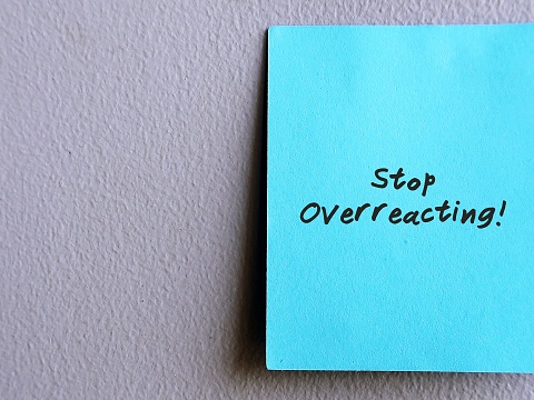 Blue note stick on wall with text written STOP OVERREACTING, refers to those who upset angry or overly defensive , react in a bigger way than normal - self reminder to control overreaction