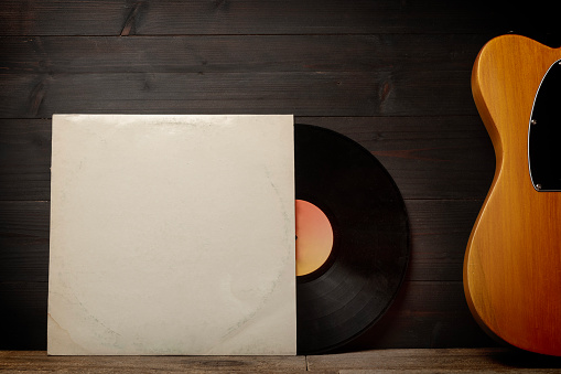 Blank cardboard record sleeve and a guitar on wood wall