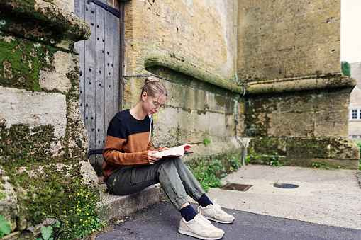 Teenage girl is sightseeing Stow-on-the-Wold, a beautiful village in Cotswolds, Gloucestershire, United Kingdom. She is sitting at the doorstep of an old church and reading a book.

Shot with Canon R5