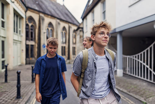 Teenagers are sightseeing Bath, a beautiful, historic town in Somerset, United Kingdom. They are walking in the small street near the Holy Trinity Church.\nShot with Canon R5