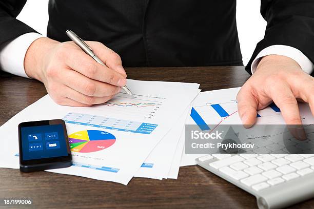 Geschäftsmann Im Büro An Tisch Mit Grafiken Und Telefon Stockfoto und mehr Bilder von Ausrüstung und Geräte