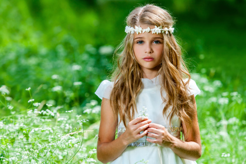 Portrait of cute blond girl dressed in white standing in green field.