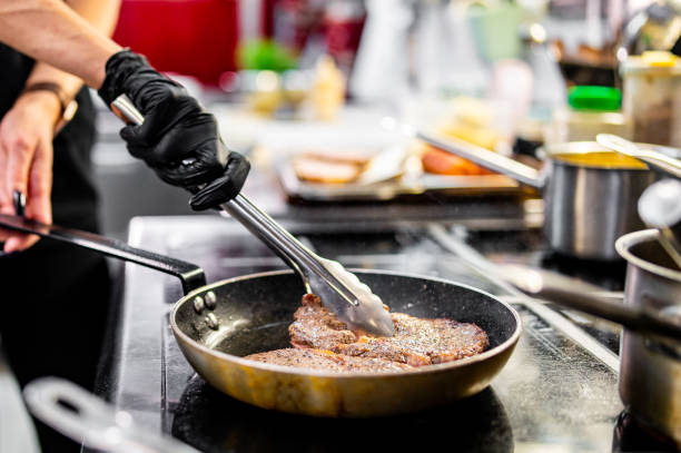 istock Professional chef cooking beef steak in frying pan on stove in restaurant kitchen 1872008619