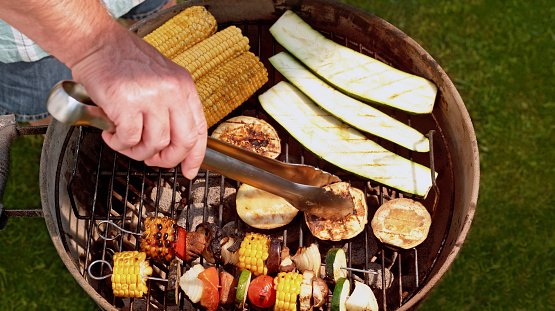 Overhead view of man hand holding tongs while cooking vegetables on grill.