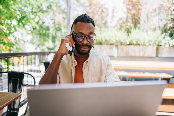 istock Mid adult man working talking on phone and using laptop at coffee shop 1872011137