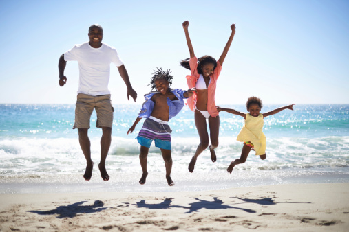 An excited family of four jumping into the air on the beach