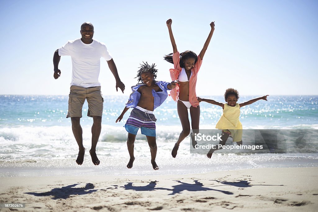 Woohoo! Vacation time rocks! An excited family of four jumping into the air on the beach Family Stock Photo