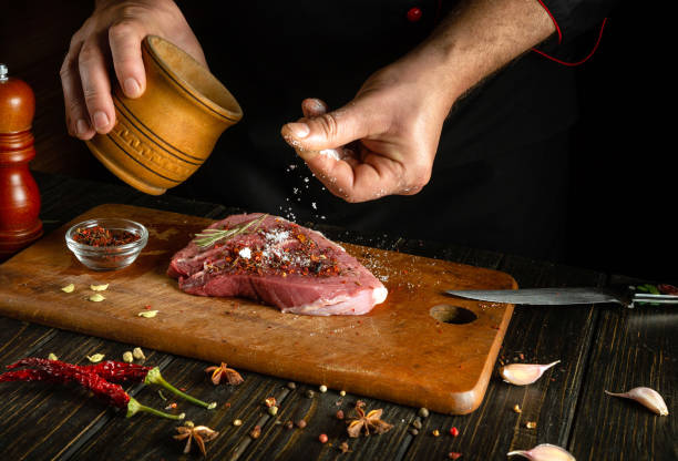 istock The chef sprinkles salt on the raw meat. Preparing beef steak before baking. Working environment in a restaurant or cafe kitchen 1872028297