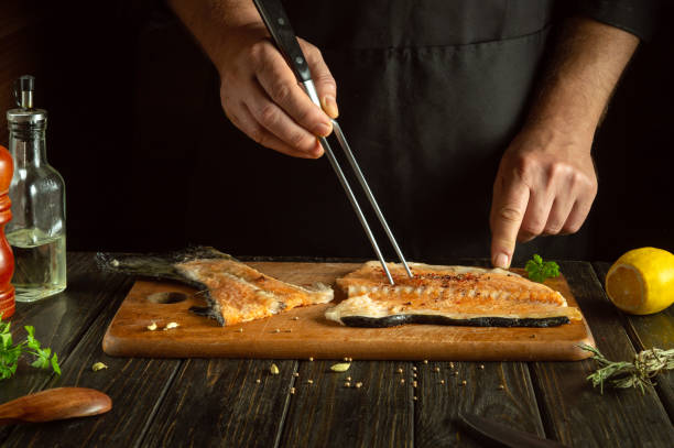 istock Chef preparing fresh fish steak on the kitchen table. Salmon is a delicious fish for preparing lunch or breakfast. Fork in the hand of the cook 1872029785