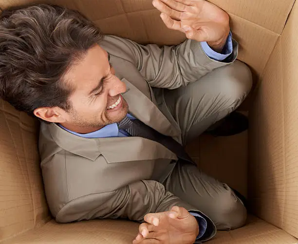 Concept shot of a young businessman trapped in a cardboard box