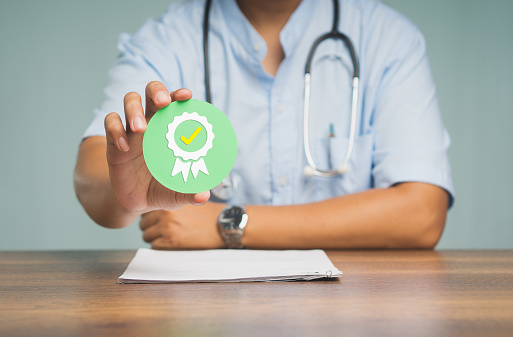A Physician holding a quality assurance symbol while sitting at the table in the hospital. Quality assurance concept. Close-up photo.
