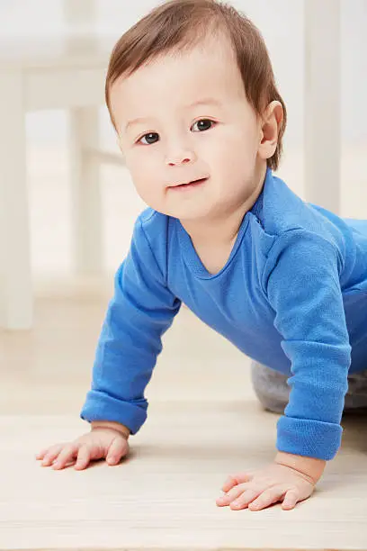 Closeup portrait of an adorable baby boy crawling on the floor and smiling at the camera