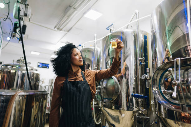 istock Quality controller young woman analyzing a glass of beer at brewery 1872068938