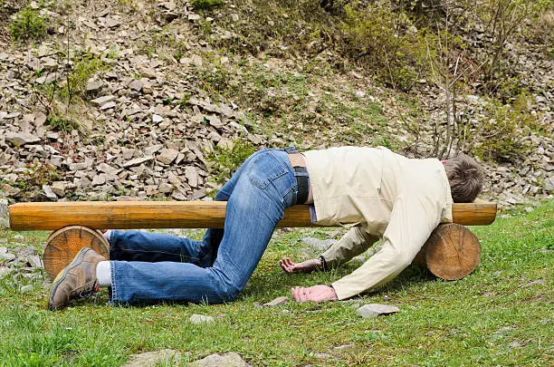 Young man deeply sleeping or drunk, laying outdoors on a wooden park bench. Profile view