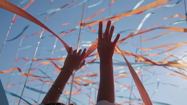 Woman hands on the background of developing ribbons from the wind. Arm gestures of victory or celebration, activites or protests