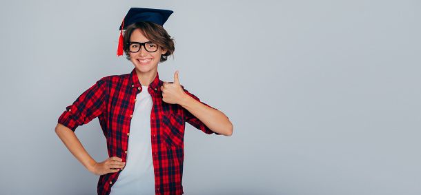 Learning is cool! Advertising banner of a cute and happy graduate in glasses and a master's graduation cap shows a finger up. University, study, education, college, classes, knowledge, graduation.