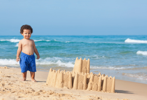 Adorable little boy playing on beach, building sand castle.