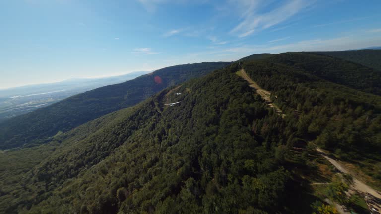 Airplane gliders flying above forests and hills with a mountain lift