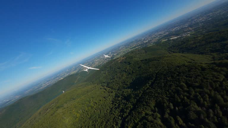 Airplane gliders flying above forests and hills with a mountain lift and a dirt road