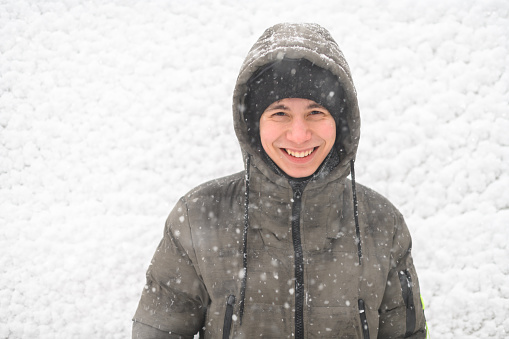 a boy is posing on snow background outdoor, it is snowing, a blizzard and frost on a winter day