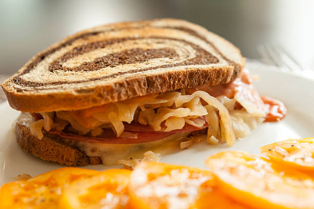 Reuben Sandwich Close-up Close up of a reuben sandwich on a plate along with a sliced heirloom tomato. reuben sandwich stock pictures, royalty-free photos & images