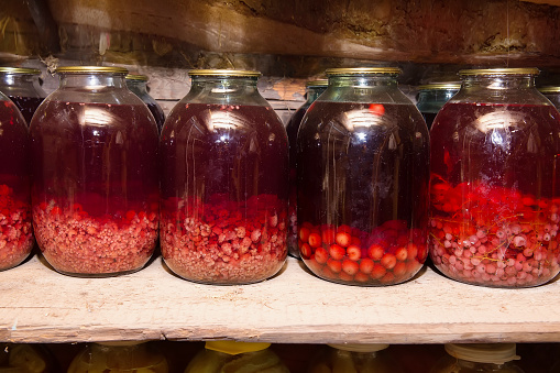 Jars of berry compote stand on a wooden shelf in the cellar of a village house.